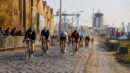 Road cyclists racing over cobbles near an industrial port district