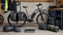 Loaded utility e-bike with panniers, cargo bags, and a floor scale in a garage.