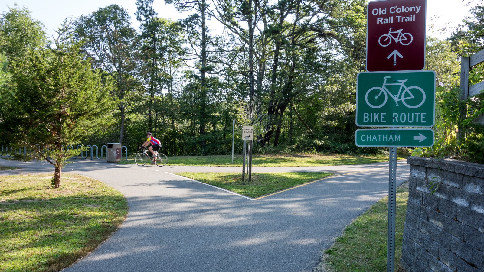 A cyclist riding near an Old Colony Rail Trail bike route sign.