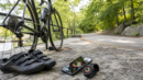 Bicycle, cycling shoes, phone, and fitness watch beside a park path.