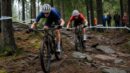 Two mountain bikers racing through a technical forest trail