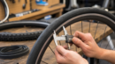 Bicycle wheel and tire being measured with calipers on a workshop bench.