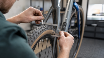 Mechanic measuring bicycle tire clearance near the frame with a ruler and gauge.