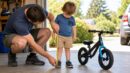 A parent measures a child's inseam beside a small balance bike.