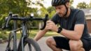 A helmeted rider checks a bicycle brake lever and front light before a ride.