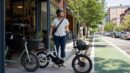 A helmeted rider standing with a compact city e-bike outside a neighborhood bike shop.
