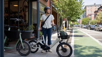 A helmeted rider standing with a compact city e-bike outside a neighborhood bike shop.