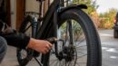 A rider checks the front tire pressure on a black e-bike with a digital gauge.