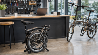 A folded commuter bike in a modern bike shop used as an editorial visual for Brompton partnership coverage.